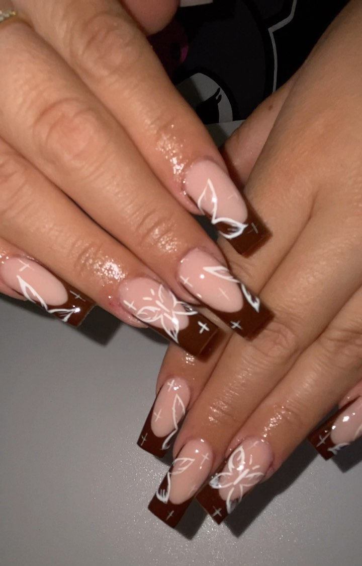 Close-up of long square nails featuring a nude base and dark chocolate Brown French Tip Nails adorned with delicate white floral line art and star accents.