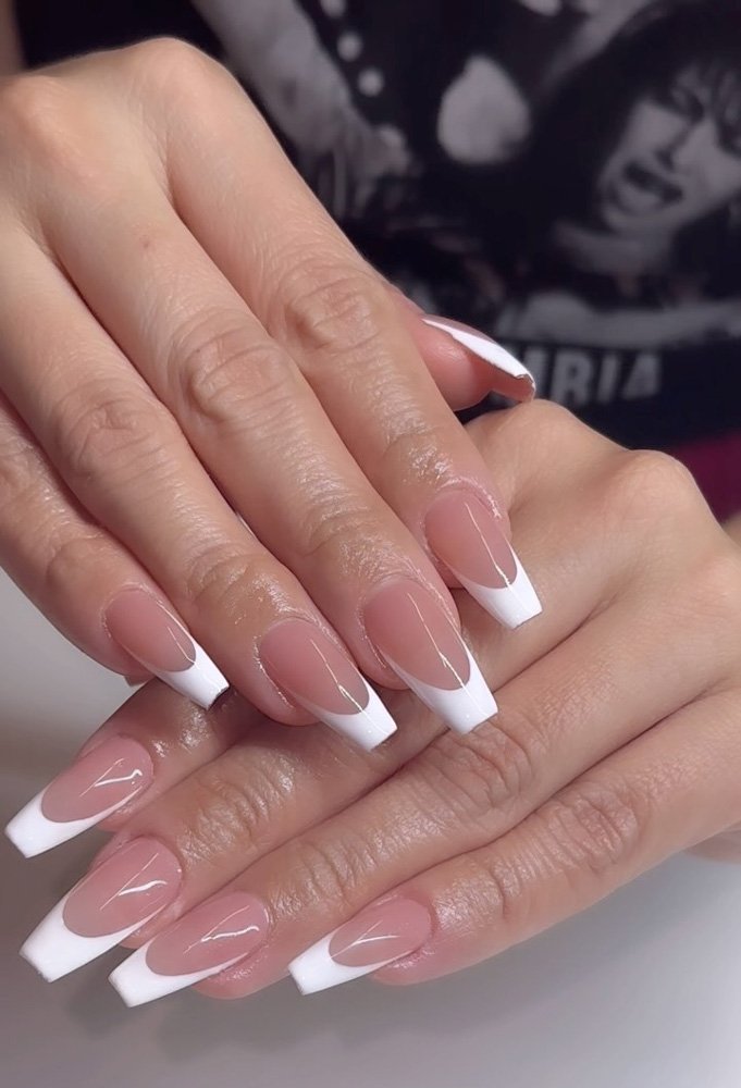 Close-up of hands featuring long, glossy nails with a nude pink base and clean white coffin French Tip Nails for a chic, modern look.