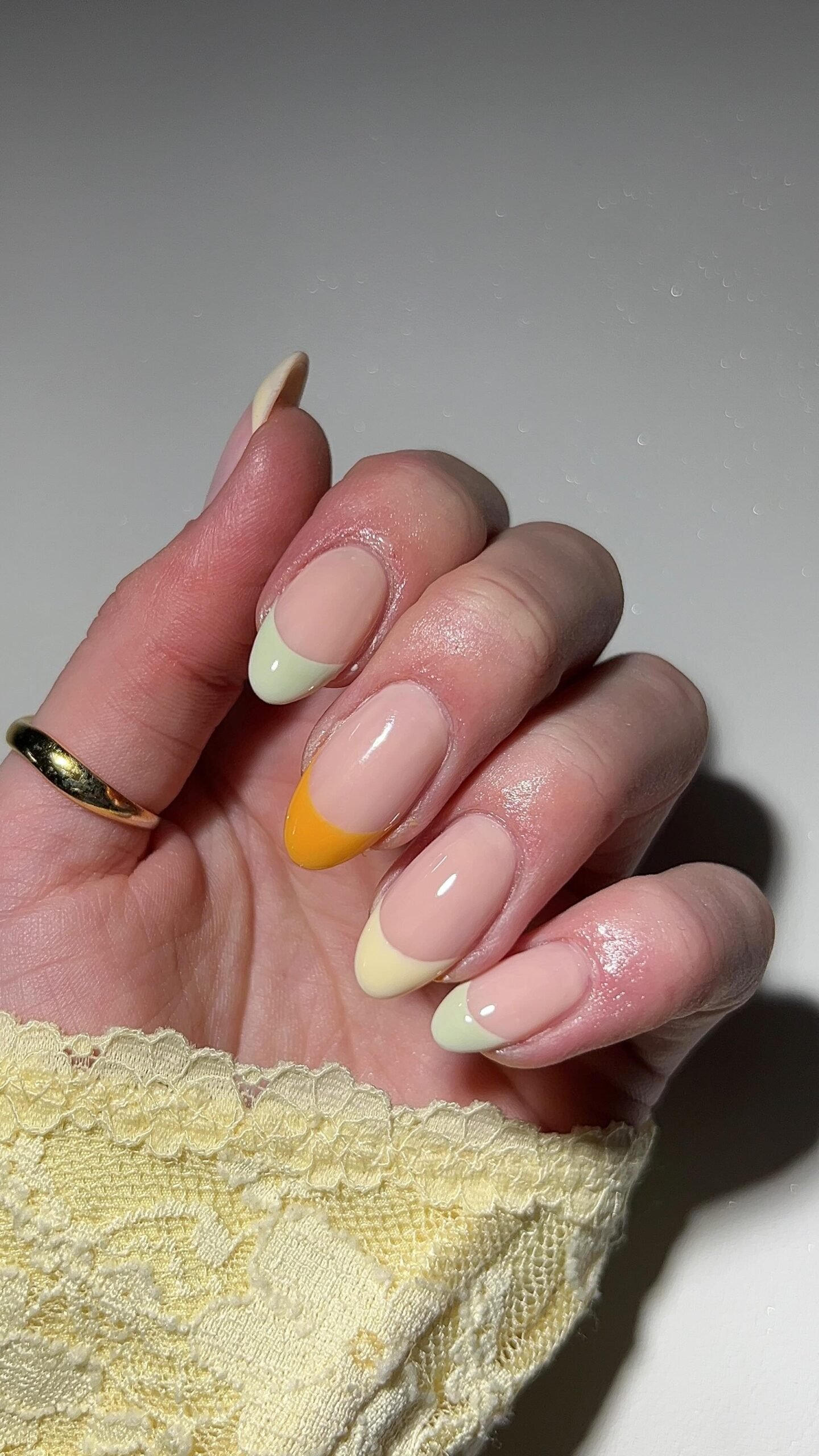 A hand with long almond nails showing a sheer nude base with soft pastel tips, highlighting a delicate style of **two color french tip nails