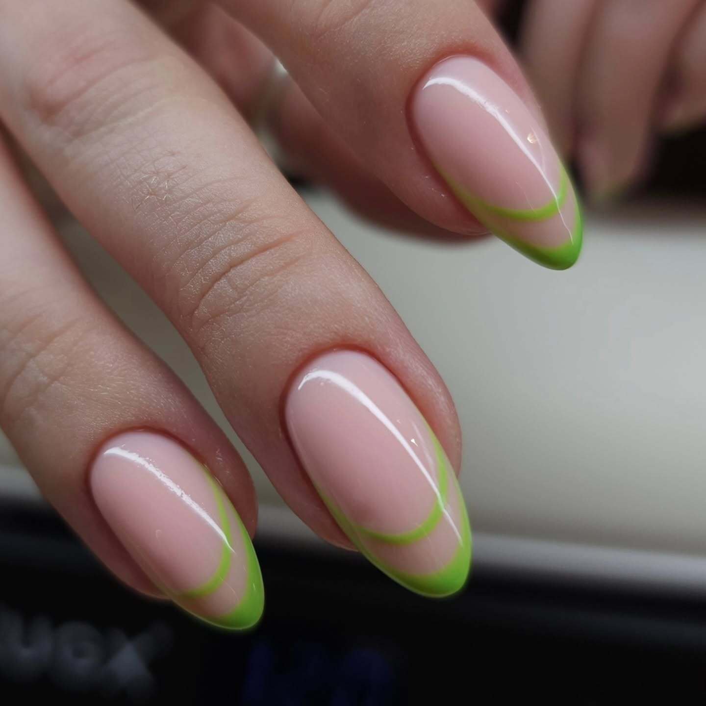 A close-up of almond-shaped nails with a sheer pink base, featuring a bold lime green tip and a matching inner curve, showcasing trendy double french nails.