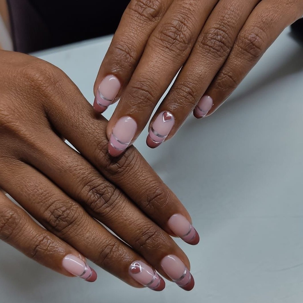 Hands with a beautiful manicure featuring soft pink nails with burgundy and white tips, showcasing elegant Double French Tip Nails accented with delicate heart designs on select fingers.