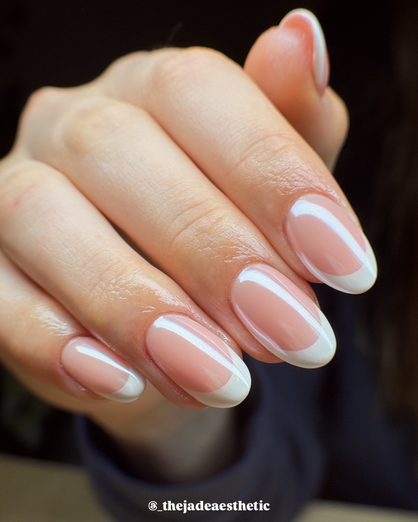 A close-up of a hand with glossy, almond-shaped nails featuring a sheer pink base and crisp white tips, exemplifying a classic glazed french tip nails style with a modern white line accent.