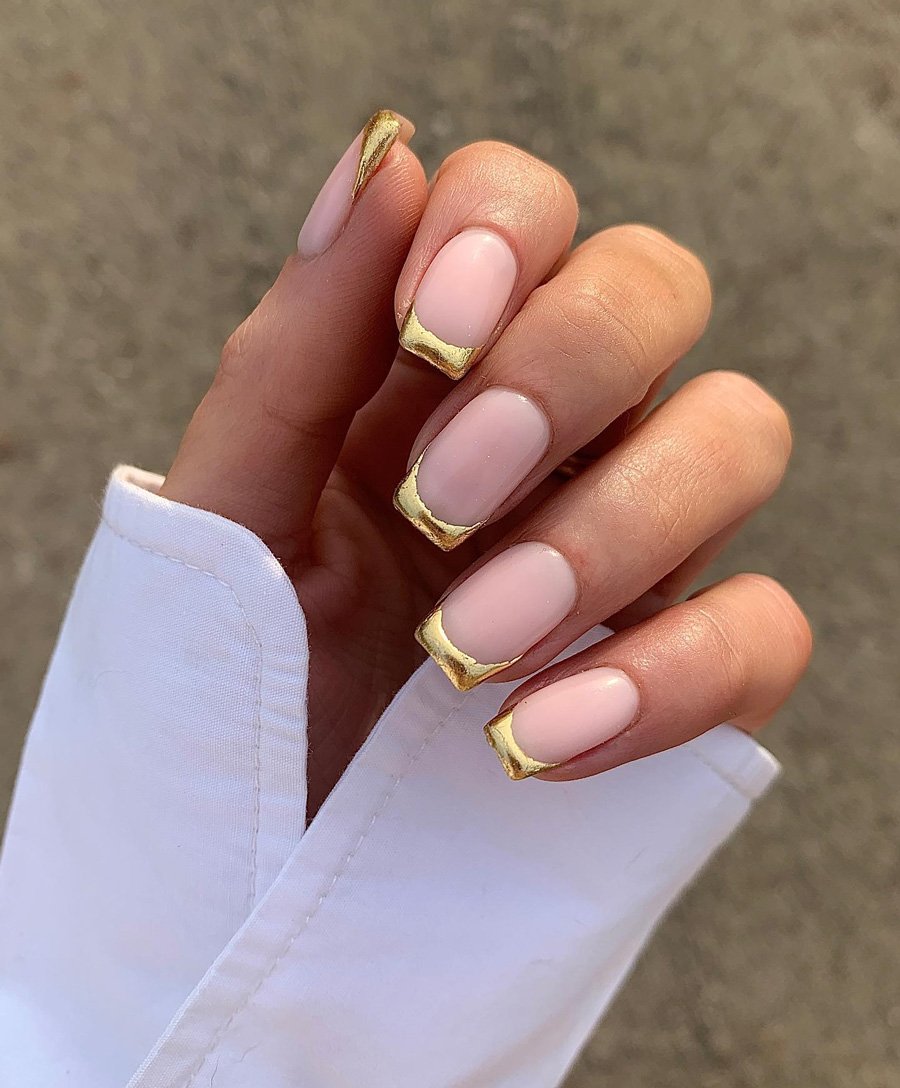 A hand with square nails featuring a soft nude base and bold, thick gold tips, showcasing stylish Gold French Tip Nails against a white shirt cuff.
