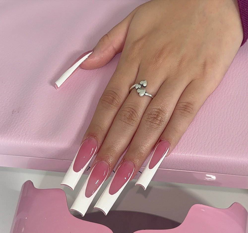 A close-up of a hand featuring extra-long, square-shaped nails with a sheer pink base and dramatic white tips, showcasing a bold style of long french tip nails.