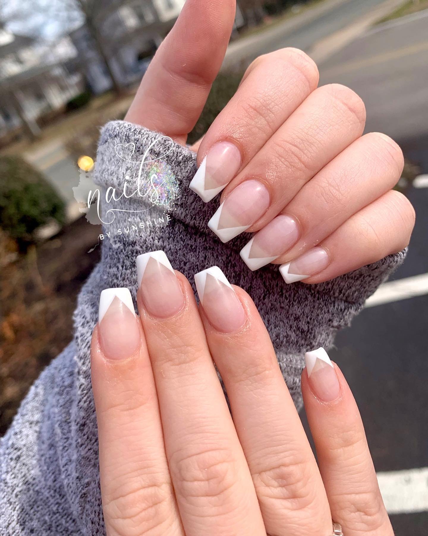 A hand in a grey sweater showing short square nails with a natural pink base and classic white v shaped french tip nails for a chic chevron look.