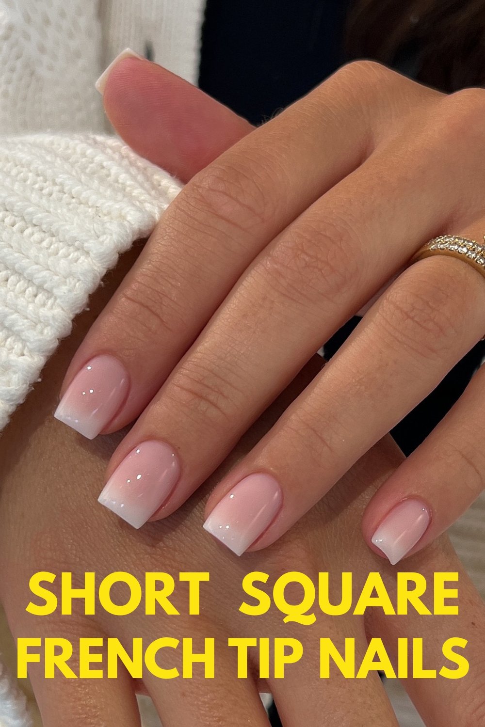 A close-up of a hand showcasing short square French tip nails ideas with a glossy nude base and white tips, styled with a white chunky knit sweater and a gold ring. Bold yellow text overlay reads "SHORT SQUARE FRENCH TIP NAILS".